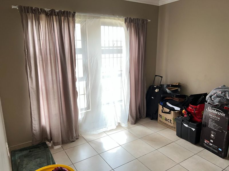 A simple living area featuring neutral tiled flooring and a window fitted with security bars, offering a blank canvas for personalization.