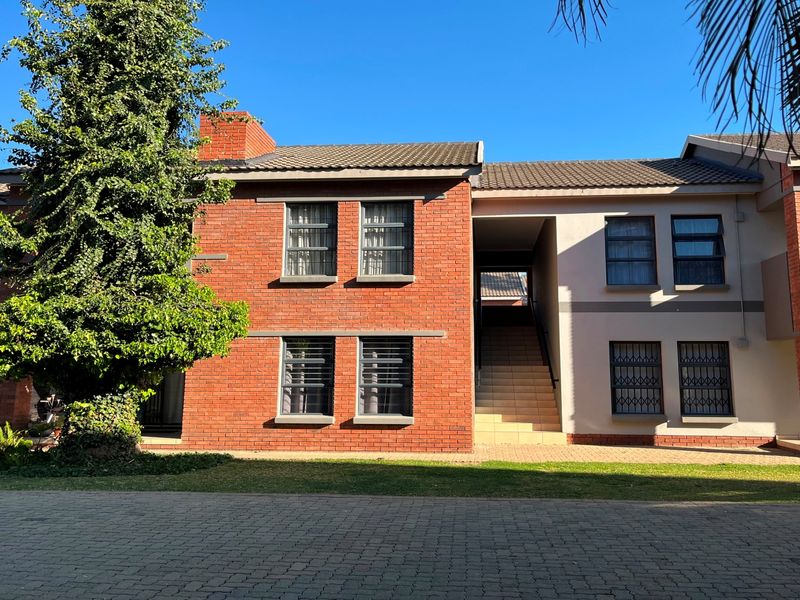 Front elevation of a multi-story brick apartment building featuring a paved driveway, tiled roof, and secure window grilles.