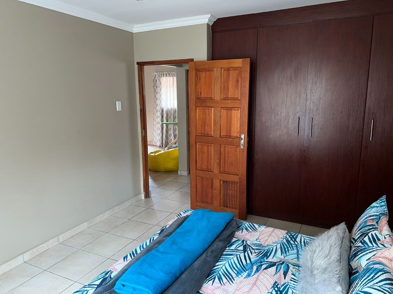 A bedroom featuring tiled flooring, built-in wooden cupboards, and a solid wooden door leading to an adjacent room.