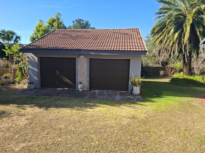A detached double garage featuring brown sectional doors and a pitched tiled roof, situated in a landscaped garden setting.