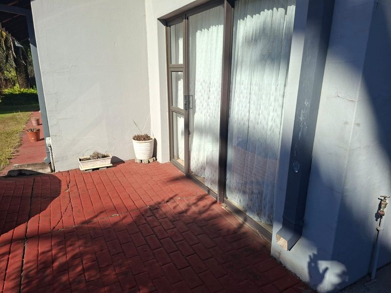 A paved outdoor patio area featuring a sliding glass door entrance, showing signs of wear on the brickwork and exterior wall plaster.