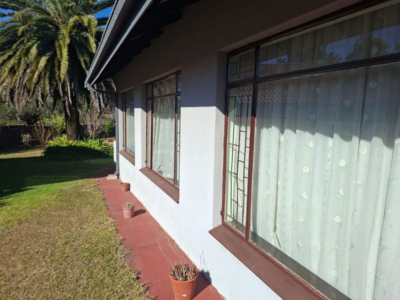 A view of the rear exterior facade featuring a painted concrete pathway, metal security window bars, and a tiled roof.