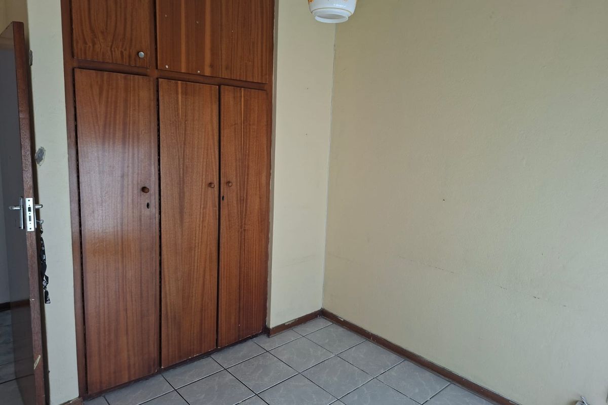 A vacant bedroom featuring built-in wooden cupboards, tiled flooring, and a neutral wall finish, offering a blank canvas for renovation.
