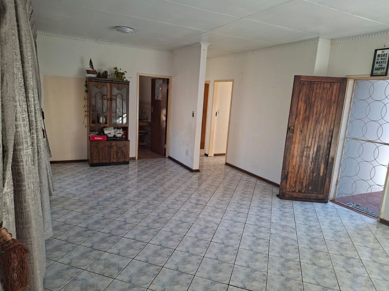 Spacious living area featuring tiled flooring, a wooden entrance door with security gate, and neutral wall finishes.