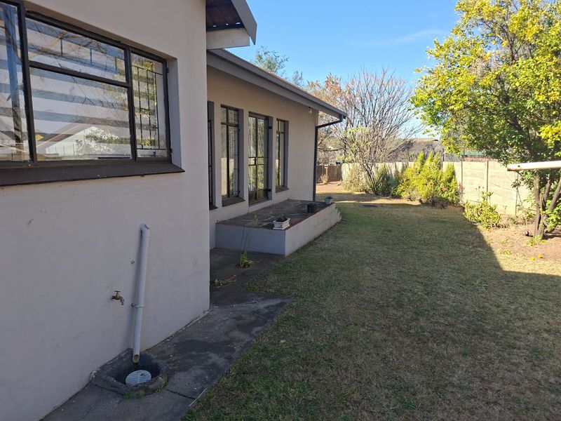 Rear view of the property featuring a concrete patio, steel-framed windows, and a private garden area with a boundary wall.