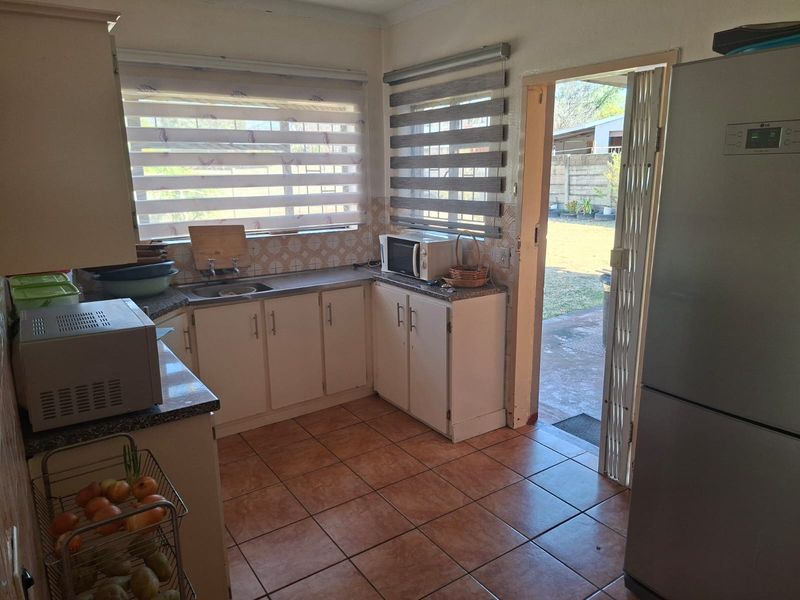 A functional kitchen featuring tiled flooring, built-in cabinetry, laminate countertops, and direct access to the rear garden through a security gate.