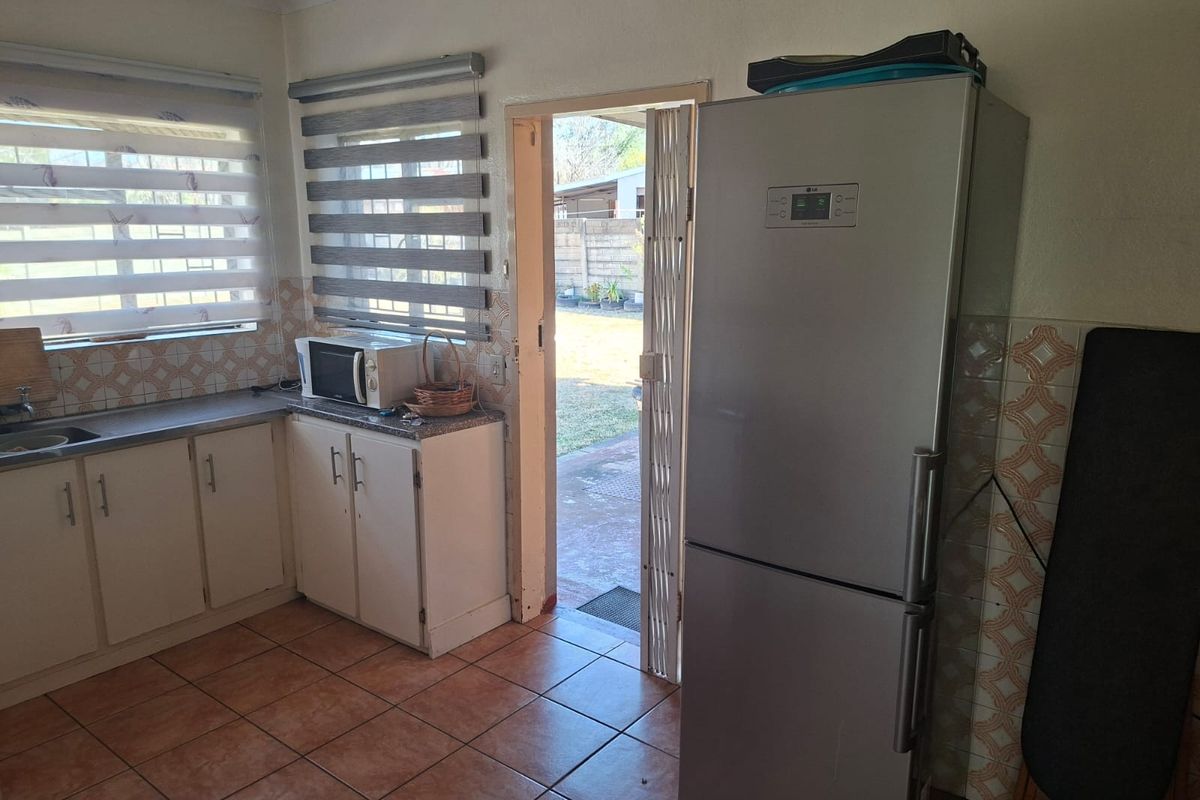 Functional kitchen featuring built-in cabinetry, tiled backsplash, and direct access to the rear garden area through a security gate.