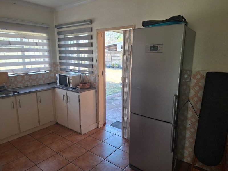 Functional kitchen featuring built-in cabinetry, tiled backsplash, and direct access to the rear garden area through a security gate.
