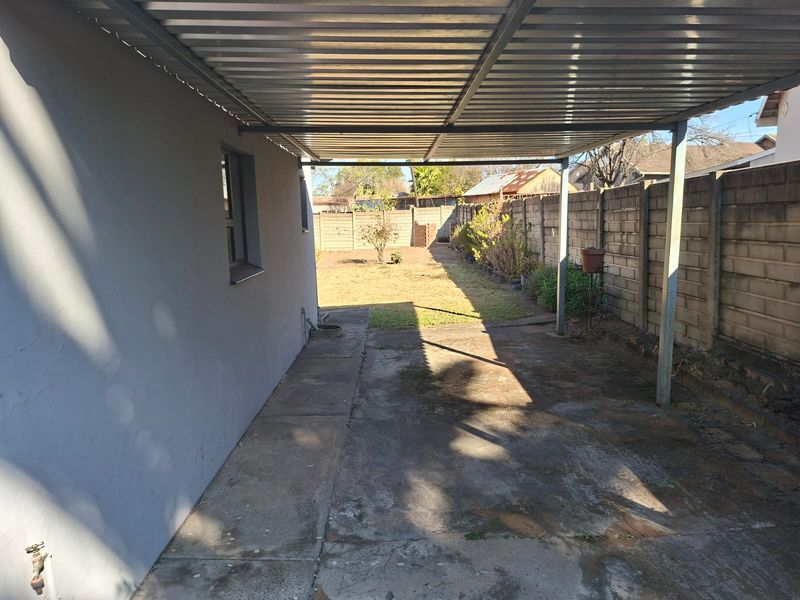 A covered outdoor patio area featuring a corrugated metal roof, concrete flooring, and a private rear garden enclosed by a precast concrete wall.
