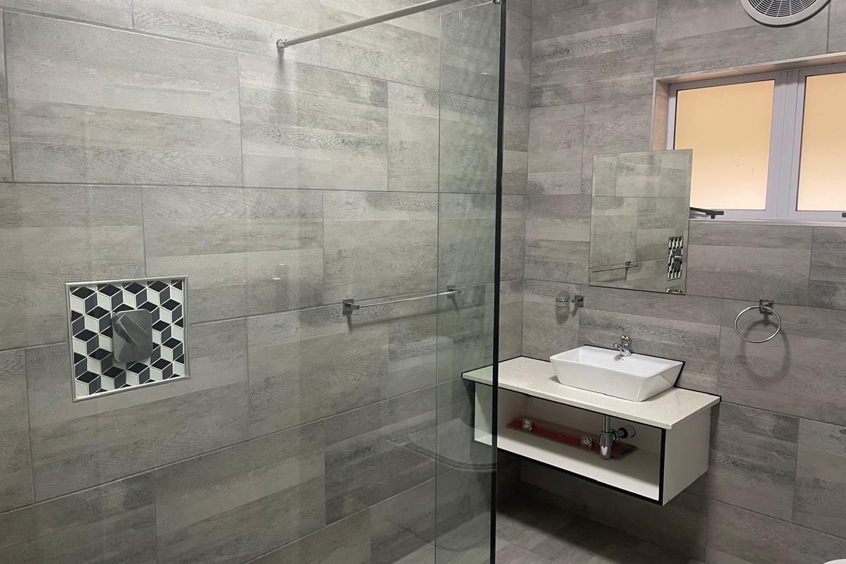 Modern bathroom featuring grey wood-look wall tiles, a glass shower screen, a wall-mounted vanity with a vessel sink, and a recessed shower niche.