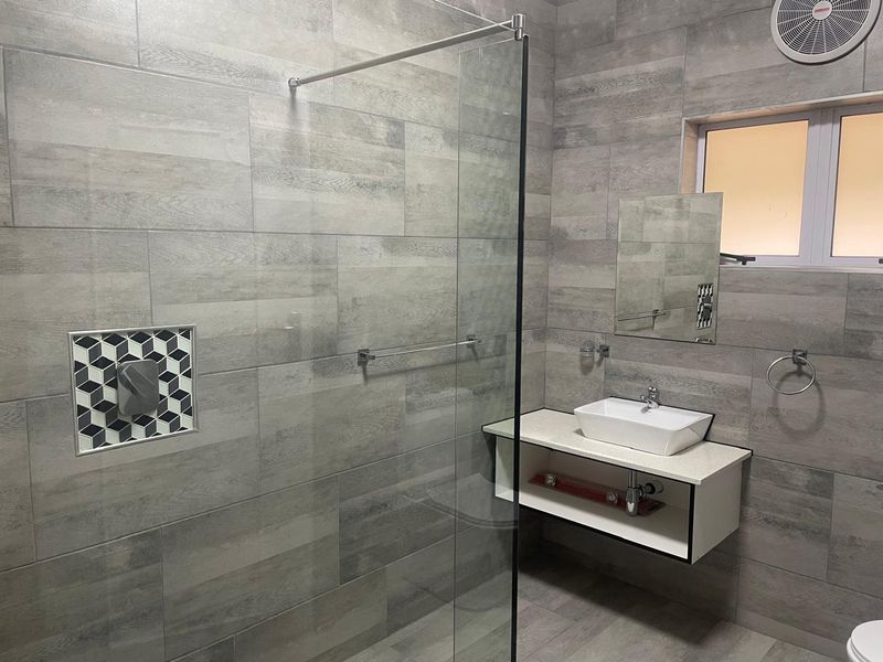 Modern bathroom featuring grey wood-look wall tiles, a glass shower screen, a wall-mounted vanity with a vessel sink, and a recessed shower niche.