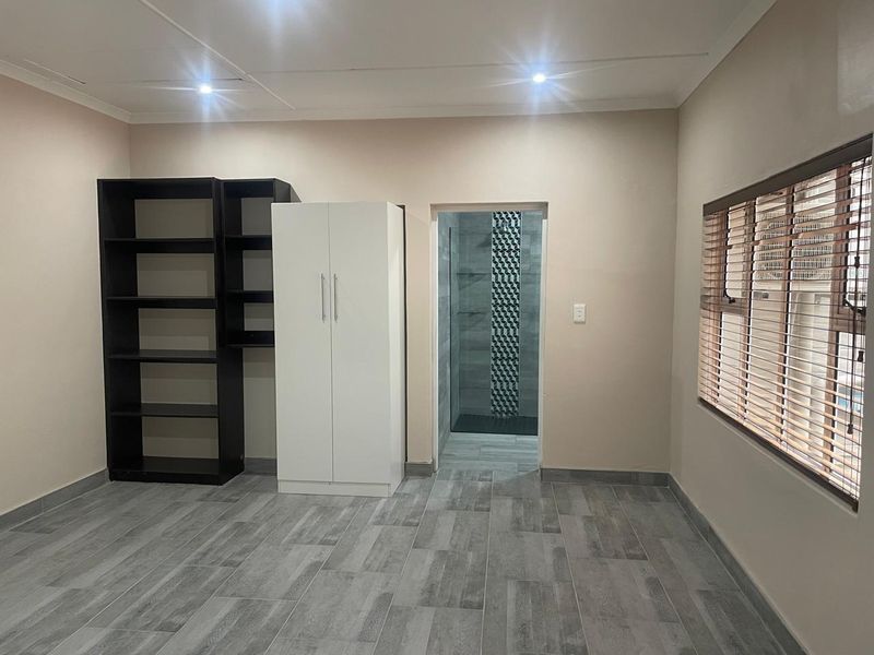 A well-maintained bedroom featuring modern grey tiled flooring, recessed lighting, venetian blinds, and direct access to an en-suite bathroom.