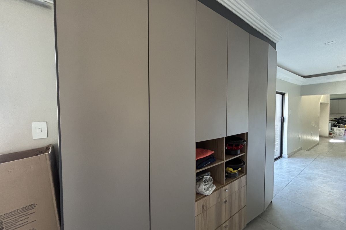 A modern bedroom featuring floor-to-ceiling built-in cabinetry with a mix of solid doors and open shelving, complemented by neutral tiled flooring.