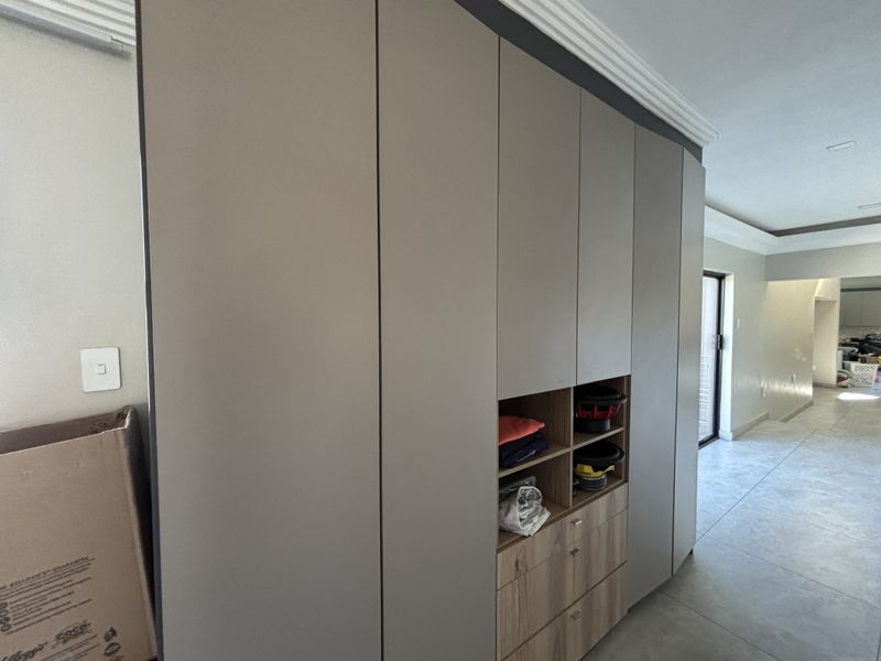 A modern bedroom featuring floor-to-ceiling built-in cabinetry with a mix of solid doors and open shelving, complemented by neutral tiled flooring.