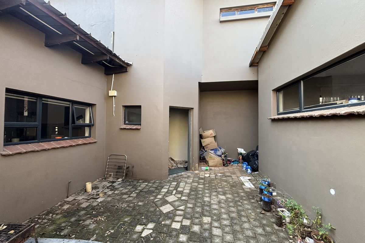 A rear courtyard area featuring paved flooring and aluminium window frames, requiring maintenance and cleaning to improve the outdoor space's appeal.