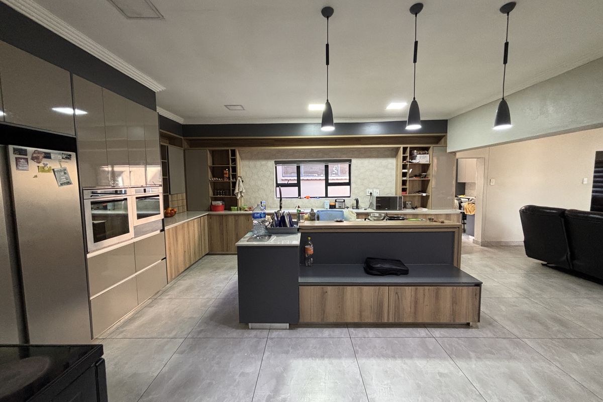 Modern open-plan kitchen featuring sleek cabinetry, a central island with integrated seating, built-in oven, and contemporary pendant lighting over the workspace.