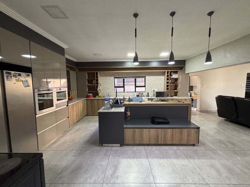 Modern open-plan kitchen featuring sleek cabinetry, a central island with integrated seating, built-in oven, and contemporary pendant lighting over the workspace.