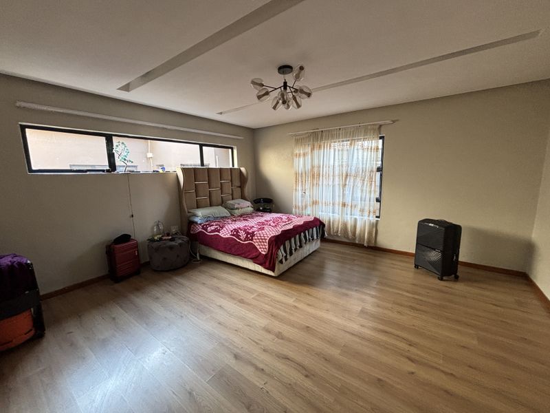 Spacious bedroom featuring light wood-look laminate flooring, a modern ceiling light fixture, and large windows with aluminium frames.
