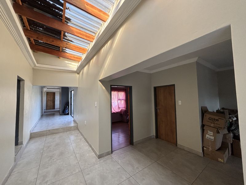 Spacious hallway featuring tiled flooring and a large skylight with timber beams, providing ample natural light and access to multiple rooms.