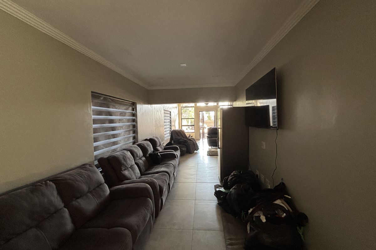 A spacious living room featuring tiled flooring, recessed ceiling lighting, and large windows with roller blinds, offering a functional and well-lit living space.