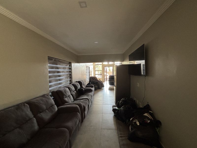 A spacious living room featuring tiled flooring, recessed ceiling lighting, and large windows with roller blinds, offering a functional and well-lit living space.