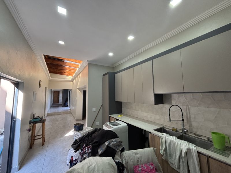 A functional laundry area featuring modern built-in cabinetry, a stainless steel sink, and a bright, airy atmosphere enhanced by a skylight and recessed lighting.