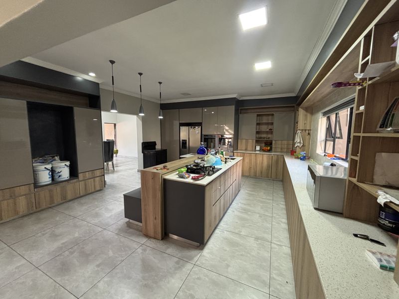 Modern kitchen featuring a large central island, stone countertops, extensive built-in cabinetry, and contemporary pendant lighting in an open-plan layout.