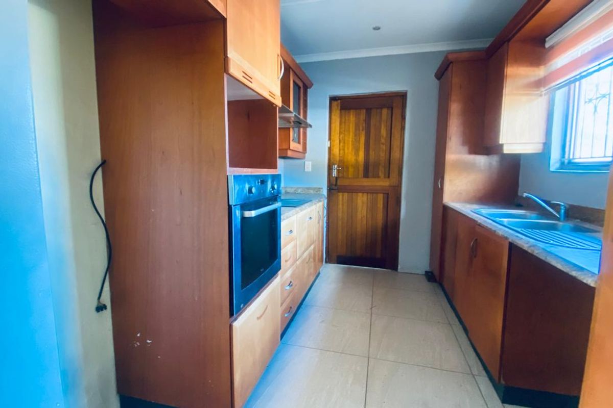 A functional kitchen featuring built-in wooden cabinetry, a built-in oven, extractor fan, and stainless steel sink, finished with tiled flooring.