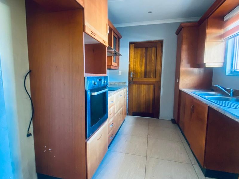 A functional kitchen featuring built-in wooden cabinetry, a built-in oven, extractor fan, and stainless steel sink, finished with tiled flooring.