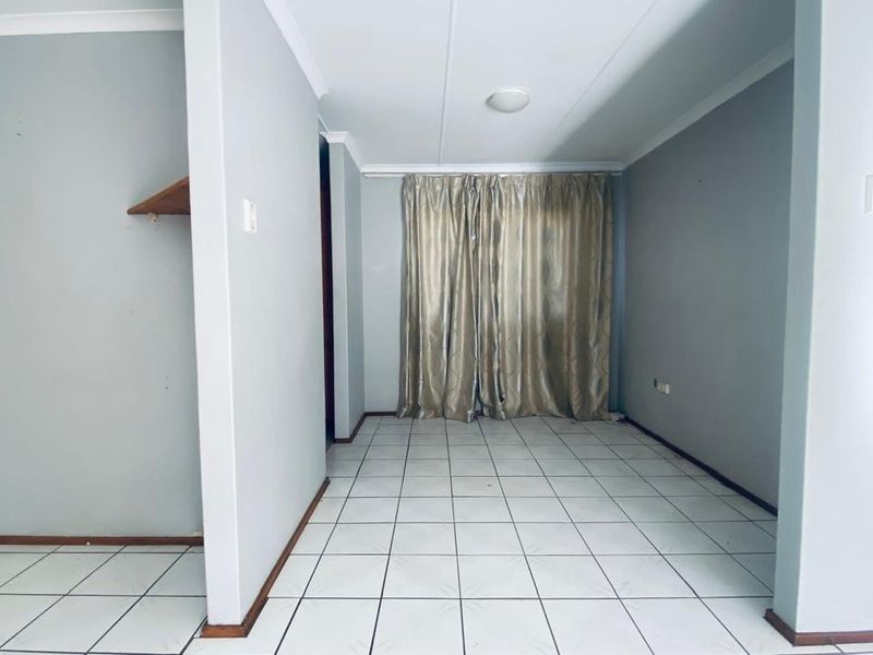An empty, neutrally painted living area featuring white tiled flooring and coved ceilings, providing a blank canvas for interior design.
