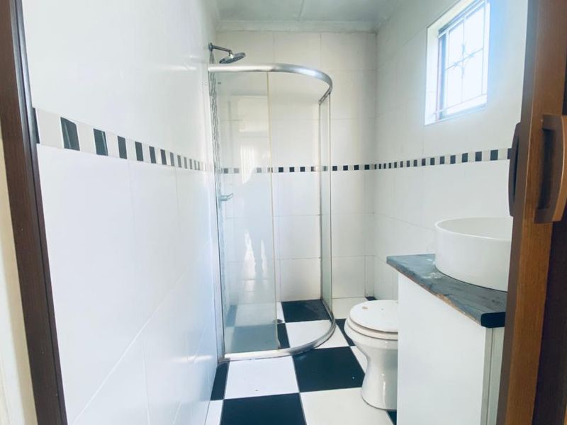 A functional bathroom featuring a corner shower enclosure, a vessel sink vanity, and a classic black and white tiled floor and wall finish.