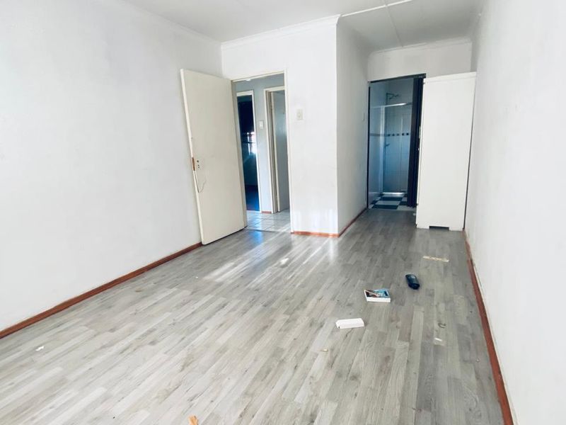 An empty bedroom featuring light-toned laminate flooring, white walls, and access to an adjoining bathroom area.