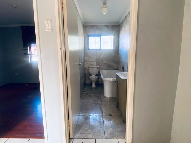 A functional bathroom featuring a bathtub, toilet, and vanity, finished with neutral wall and floor tiles.