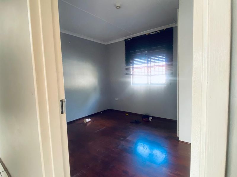 An empty bedroom featuring dark timber flooring, a window with security bars, and a built-in cupboard, ready for a fresh update.