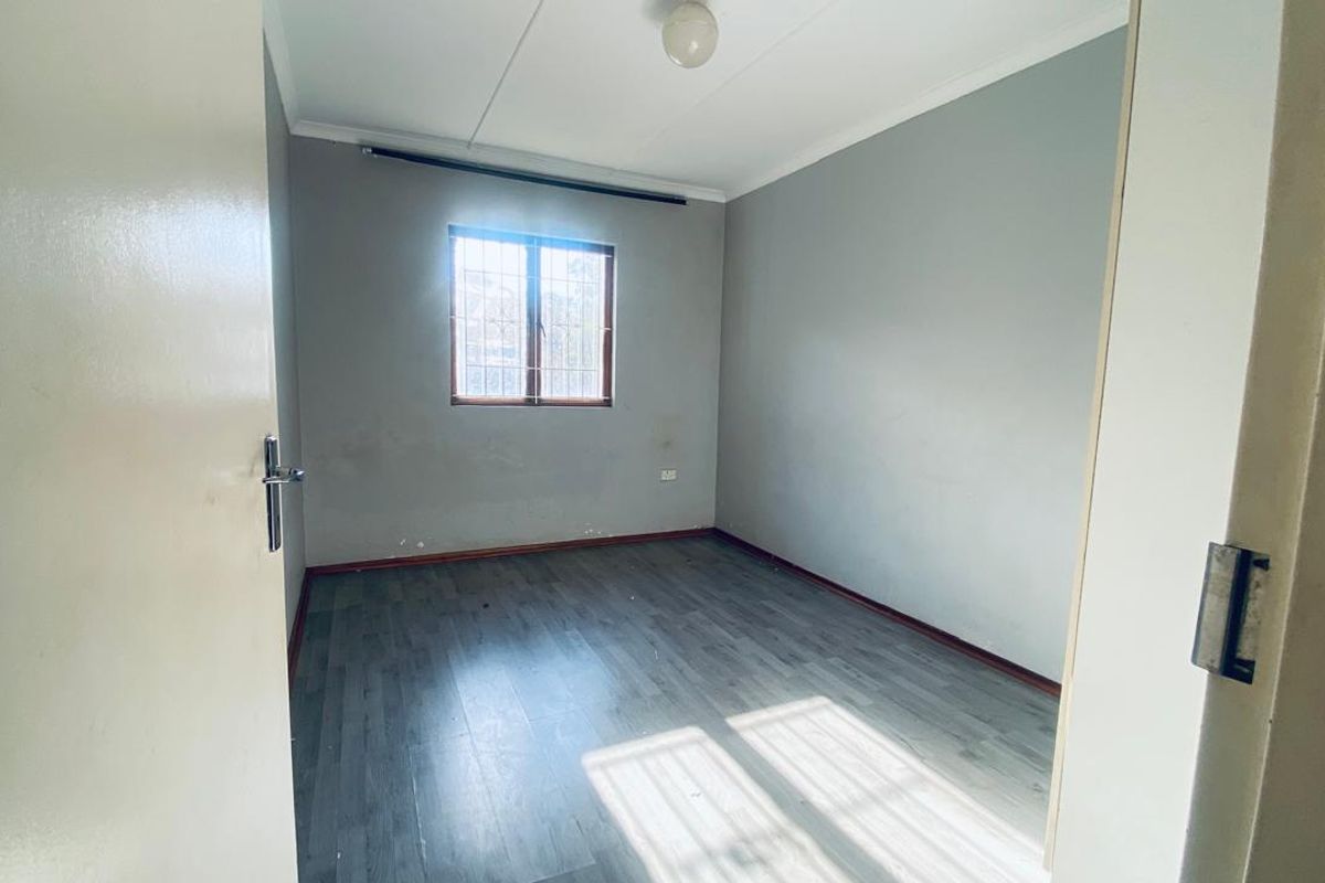 An empty bedroom featuring grey laminate flooring, neutral walls, and a window fitted with security bars.