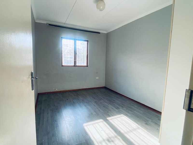 An empty bedroom featuring grey laminate flooring, neutral walls, and a window fitted with security bars.