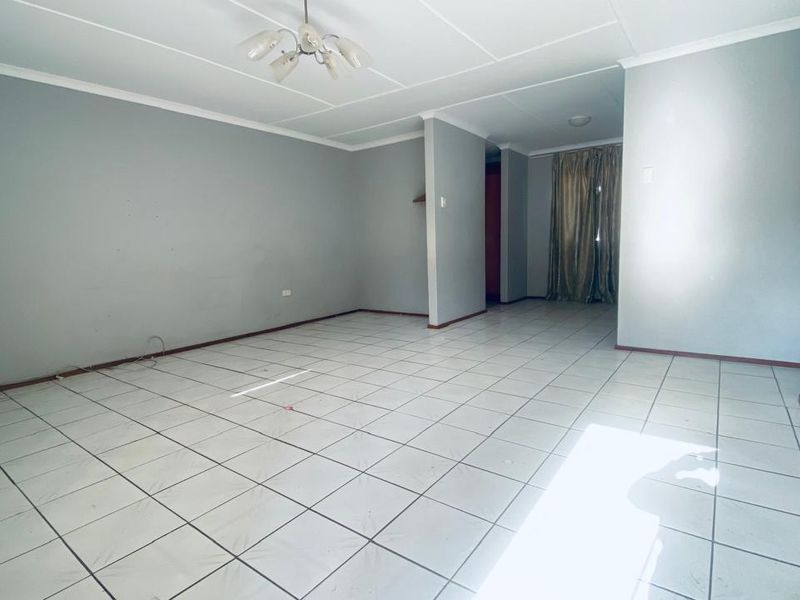 An empty, open-plan living area featuring neutral wall paint and tiled flooring, offering a blank canvas for interior design.