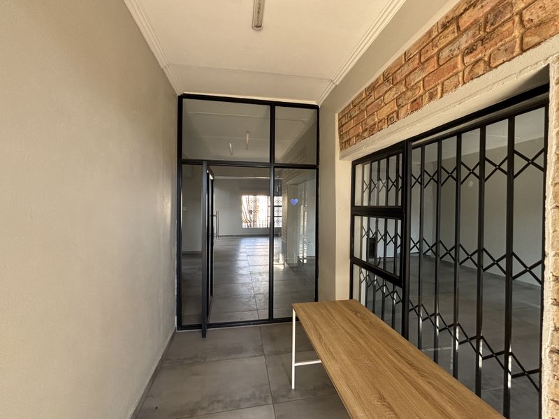 A bright entrance hall featuring tiled floors, an exposed brick accent wall, and a modern black metal framed glass door leading to the interior.
