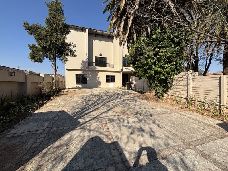 A paved driveway leading to the front facade of a multi-story house, featuring perimeter walls and a small balcony.