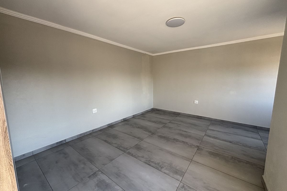 A clean, empty bedroom featuring modern large-format grey floor tiles, neutral wall paint, and a coved ceiling with a flush-mount light fixture.