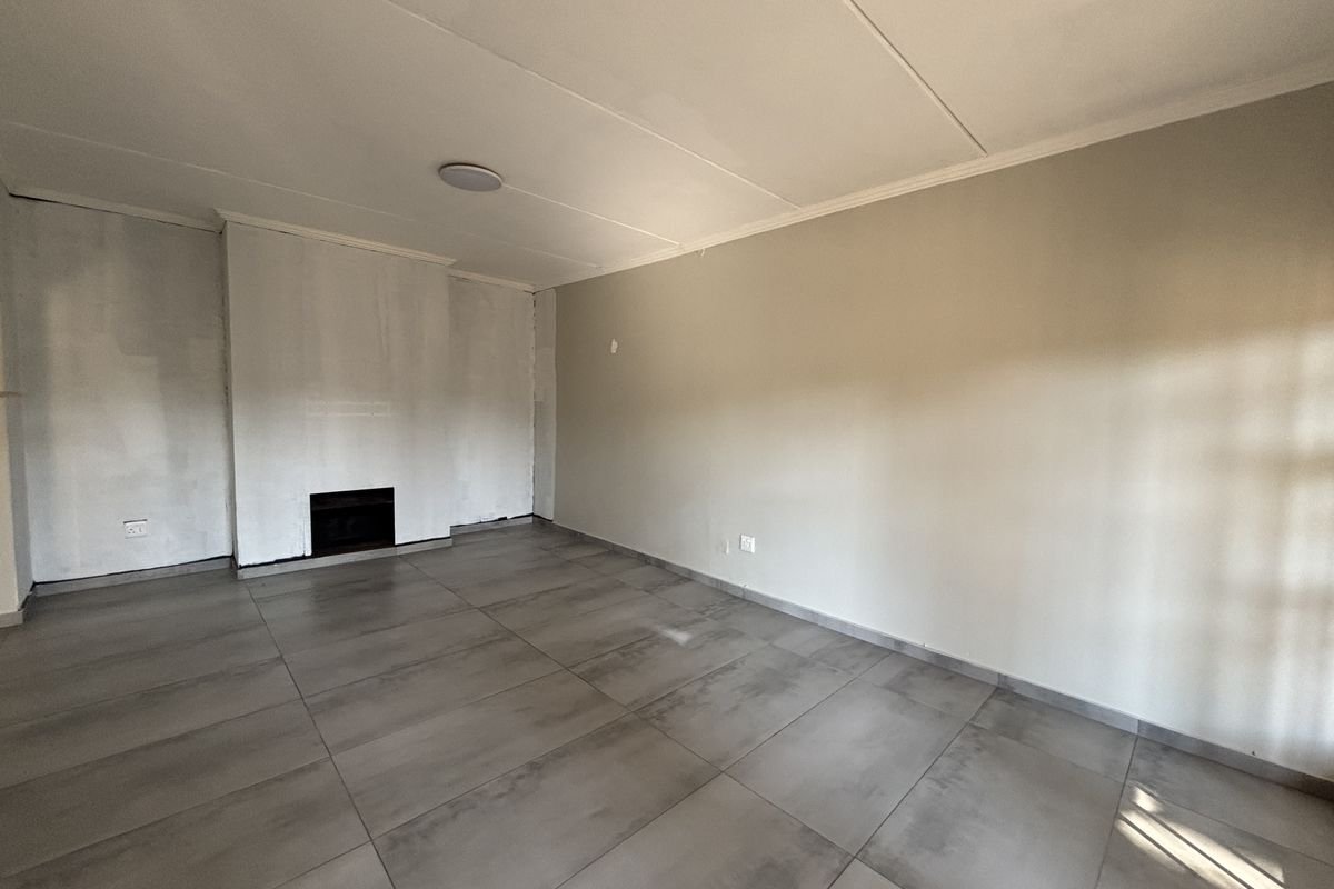 An empty living room featuring large format floor tiles and a built-in fireplace, currently undergoing interior wall finishing.