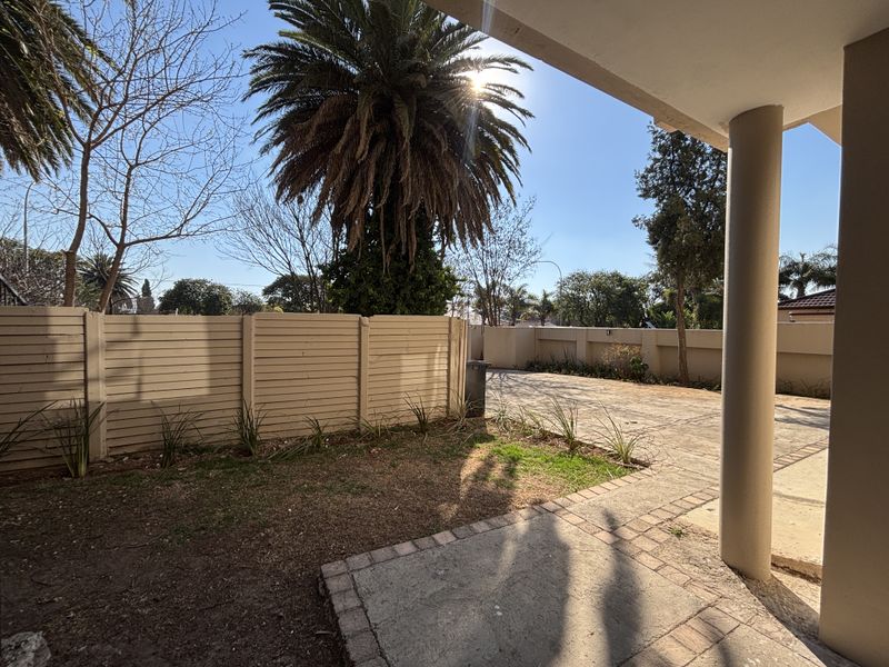 A covered patio area overlooking a paved driveway and a small garden space with precast boundary walling.