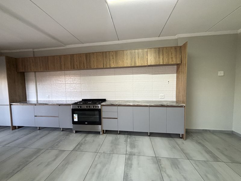 Modern kitchen featuring grey base cabinets, wood-look overhead storage, stone-effect countertops, a freestanding oven, and neutral tiled flooring.