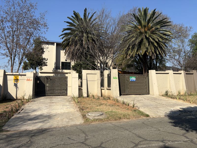 Front view of the property featuring a perimeter wall, dual driveways, and metal security gates providing access to the residence.