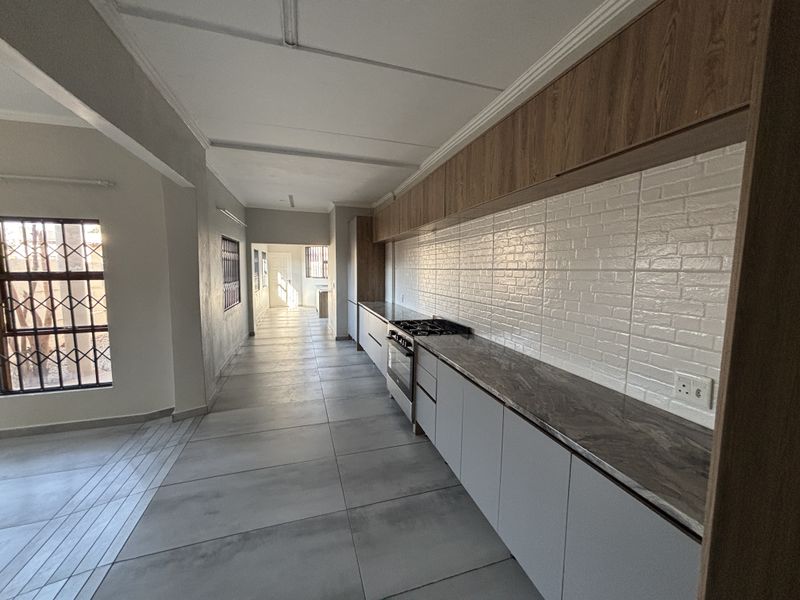 Modern galley-style kitchen featuring sleek cabinetry, stone countertops, a built-in gas hob and oven, and contemporary tiled flooring.