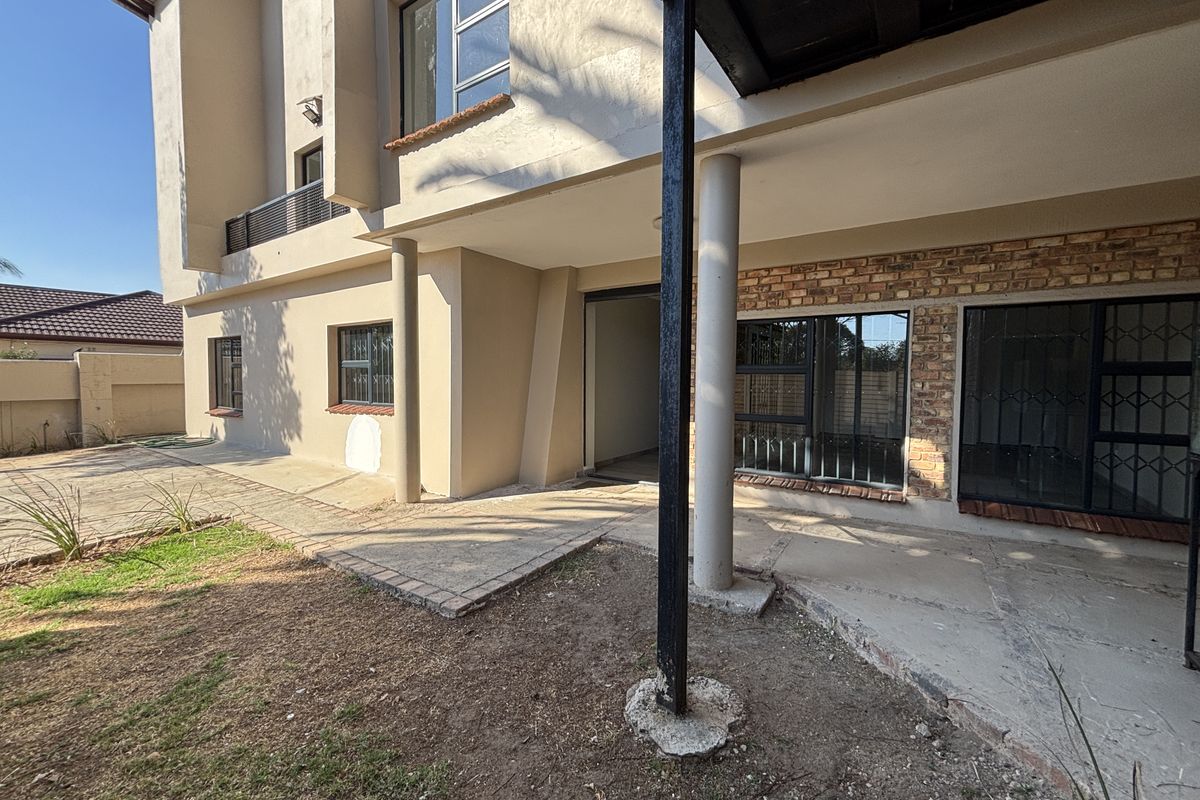 Rear exterior view of the property featuring a concrete patio area, exposed brick accents, and security-fitted windows.