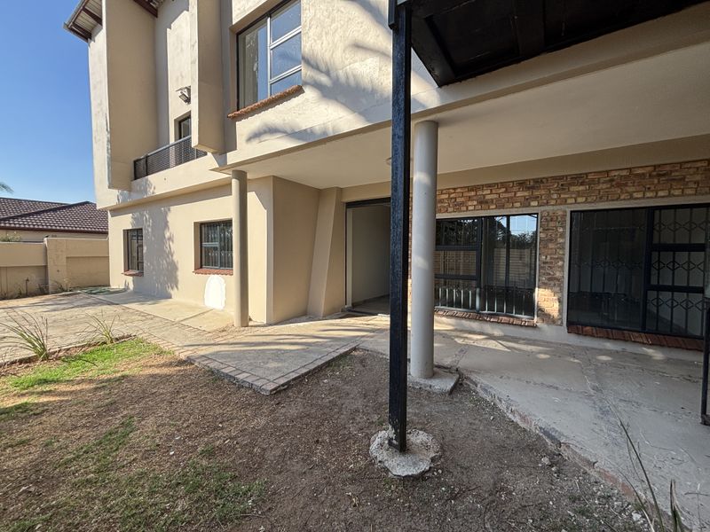 Rear exterior view of the property featuring a concrete patio area, exposed brick accents, and security-fitted windows.
