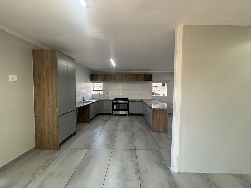 A modern, spacious kitchen featuring grey and wood-tone cabinetry, tiled flooring, a built-in stove, and ample counter space in an open-plan layout.