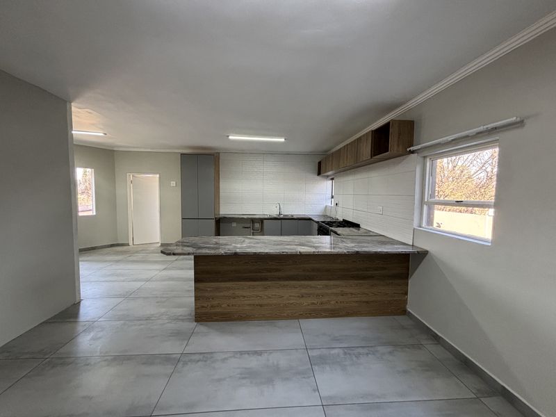 Modern open-plan kitchen featuring sleek cabinetry, stone countertops, a central island, and large format floor tiles in a neutral, contemporary finish.