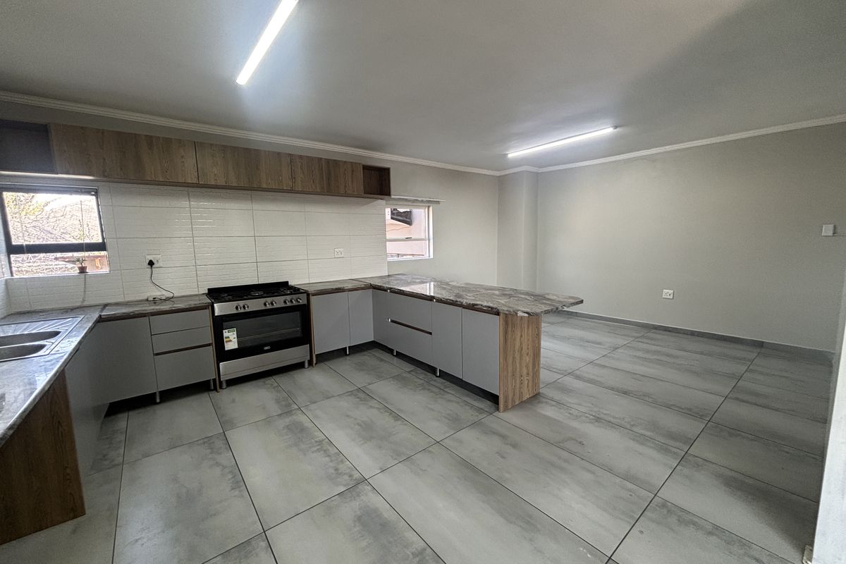 Modern open-plan kitchen featuring grey cabinetry, marble-look countertops, a freestanding stove, and large format floor tiles in a clean, vacant space.